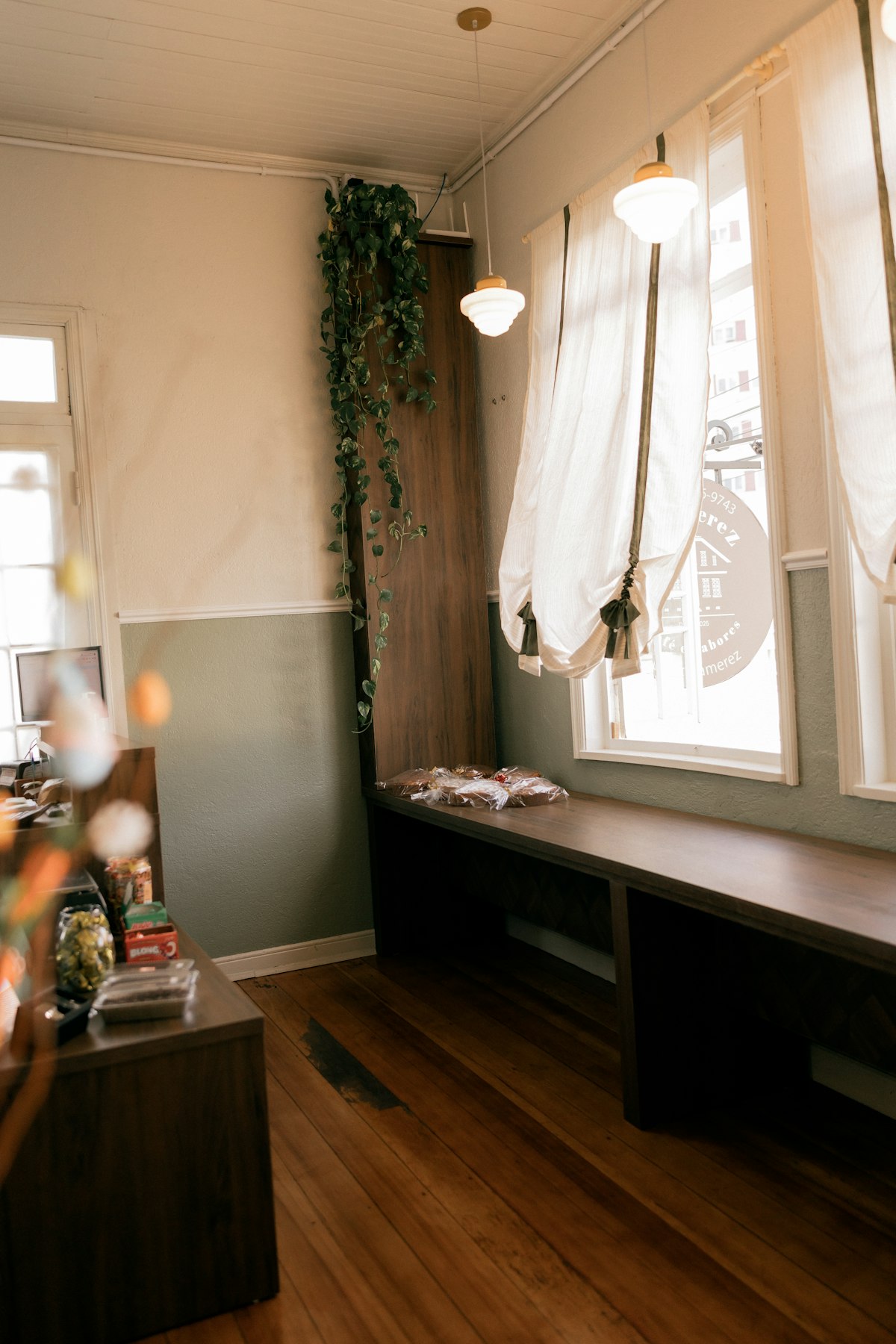 Sala clara e arejada com banco de madeira junto à janela e plantas, com bastante espaço livre